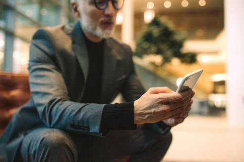 Geschäftsmann, der ein Smartphone in einer Bürolounge benutzt. Fokus auf das Mobiltelefon in der Hand eines älteren Mannes. - JLPSF16411