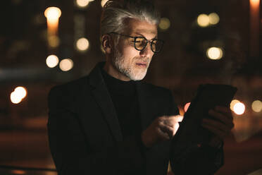 Senior business associate working on tablet computer late night in office. Mature man working overtime in office. - JLPSF16444