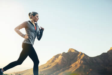Seitenansicht eines Fitness-Frau Sprint auf der Straße mit Hügeln im Hintergrund. Weibliche Athletin läuft auf der Straße am Morgen. - JLPSF16450