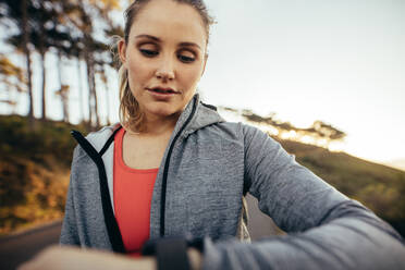 Close up of a female athlete checking time while walking on road. Fitness woman looking at her wrist watch during her morning fitness walk. - JLPSF16457