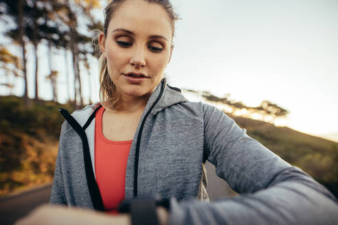 Nahaufnahme einer Sportlerin, die beim Laufen auf der Straße die Zeit überprüft. Eine Fitness-Frau schaut während ihres morgendlichen Fitness-Spaziergangs auf ihre Armbanduhr. - JLPSF16457