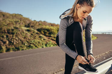 Fitness-Frau steht am Straßenrand und bindet ihre Schnürsenkel. Frau in Fitnesskleidung bindet ihre Schnürsenkel am Geländer der Straße. - JLPSF16465