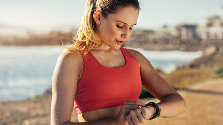 Runner woman running on beach with watch and sports bra top