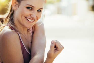Close up of a female athlete stretching her arms doing warm up exercises. Portrait of a cheerful athlete doing workout. - JLPSF16473