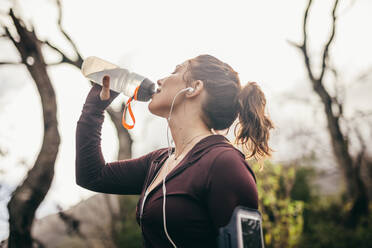 Frau trinkt Wasser nach einem Lauftraining im Freien. Eine Läuferin macht eine Pause und trinkt Wasser aus einer Flasche am Morgen. - JLPSF16475