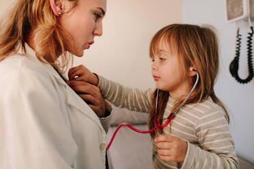 Cute girl pretending to a doctor examining the heart rate of her pediatrician at hospital. Girl patient playing with her doctor in clinic. - JLPSF16492