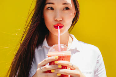 Asiatische Frau, die mit einem Strohhalm Saft aus einem Einwegplastikglas trinkt. Porträt einer jungen Frau, die ein Glas Saft trinkt. - JLPSF16538