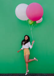 Asian woman walking holding a bunch of colorful balloons. Cheerful young woman holding balloons of different sizes. - JLPSF16546