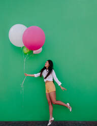 Smiling young woman holding a bunch of colorful balloons. Asian woman playing with colorful balloons. - JLPSF16547
