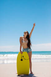 Bodyboarding enthusiast having fun at the beach on a sunny day. Happy woman standing on the beach holding a bodyboard. - JLPSF16558