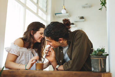 Verliebtes Paar trinkt lächelnd einen Kaffee aus einem Glas mit Strohhalm. Junger Mann und Frau genießen einen Kaffee auf dem Tisch. - JLPSF16576