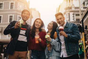 Four young asian walking in the city with fresh juice. Young friends on city street with juice. - JLPSF16584
