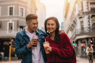 Young asian couple walking on the city street with fresh juice. Happy young man and woman on city street with juice. - JLPSF16585