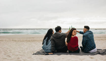 Woman sitting with friends toasting beers at the beach. Four friends partying on the beach. - JLPSF16592