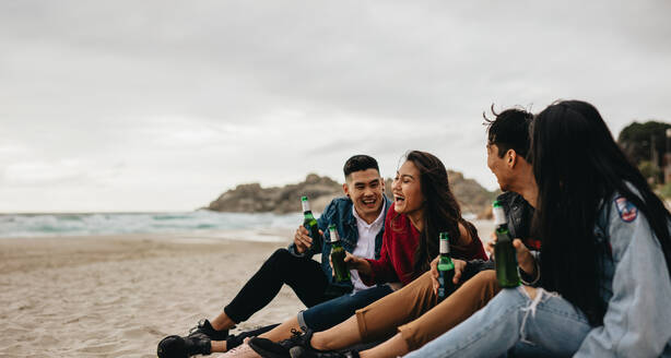 Eine Gruppe asiatischer Männer und Frauen sitzt mit einem Bier am Strand. Vier junge Freunde feiern am Strand. - JLPSF16594