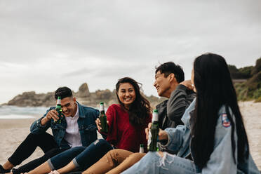 Fröhliche junge asiatische Männer und Frauen sitzen am Strand und trinken Bier. Zwei Paare feiern am Strand. - JLPSF16595