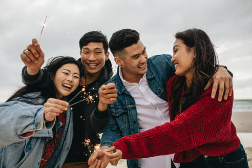 Eine Gruppe junger Leute feiert den Neujahrstag am Strand. Junge Asiaten haben Spaß mit Wunderkerzen im Freien am Meeresufer. - JLPSF16602