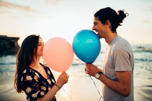 Paar bei einem Date im Freien am Strand mit Luftballon. Junger Mann und Frau mit Luftballons lächelnd am Strand. - JLPSF16605