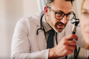 Erfahrener HNO-Arzt untersucht das Ohr eines Patienten mit einem Otoskop. Männlicher Arzt untersucht das Ohr eines Patienten mit einem Instrument in seiner Klinik. - JLPSF16617