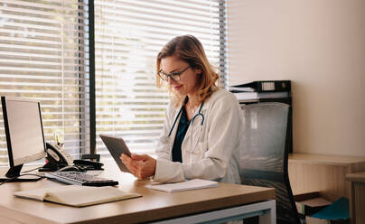 Female doctor using a digital tablet at her desk in the clinic. Female doctor working on her tablet pc in her office. - JLPSF16626