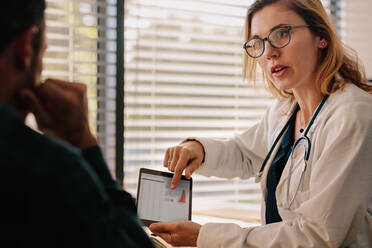 Confident female doctor talking with patient with test results on tablet. Doctor and patient talking about the treatment in hospital. - JLPSF16628