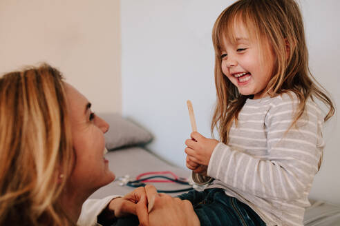 Niedliches Mädchen, das einen Zungenspatel in der Hand hält, während sie mit ihrem Arzt spricht. Mädchen, das ihren Kinderarzt zur Halsuntersuchung aufsucht. - JLPSF16643