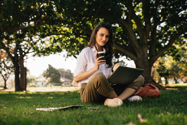 Schöne Frau sitzt im Park mit Kaffee und Laptop. Frau entspannt sich im Park. - JLPSF16644