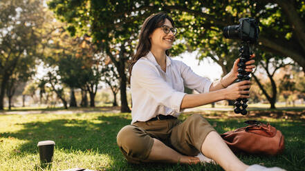 Bloggerin, die ein Video mit einer Digitalkamera auf einem flexiblen Stativ aufnimmt. Junge Frau, die in einem Park einen Vlog aufnimmt. - JLPSF16645