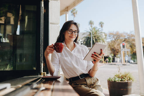 Geschäftsfrau sitzt in einem Café mit einer Tasse Kaffee und einem digitalen Tablet. Frau sitzt in einem Café mit einem digitalen Tablet und trinkt Kaffee. - JLPSF16647