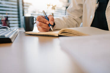 Nahaufnahme der Hände einer Ärztin, die etwas in ihr Tagebuch schreibt. Eine Ärztin schreibt Notizen über einen Patienten im Büro. - JLPSF16656