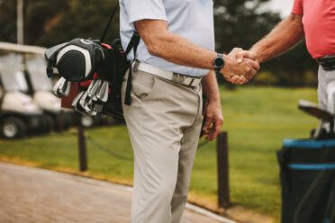 Cropped shot of senior golf players shaking hands when meeting on a golf course. Golfers greeting each other with a handshake before the game. - JLPSF16664