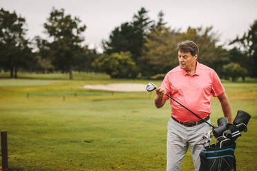 Älterer Mann holt Golfschläger aus Tasche auf Golfplatz. Älterer männlicher Golfer wählt seinen Schläger für das nächste Spiel. - JLPSF16665