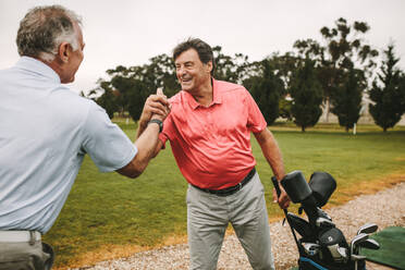 Fröhliche ältere Golfspieler schütteln sich auf der Driving Range die Hände. Zwei reife Golfspieler schütteln sich nach einer erfolgreichen Trainingseinheit auf der Driving Range die Hände. - JLPSF16667