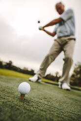 Golfball auf dem Abschlag mit einem männlichen Spieler, der einen Schlag auf der Driving Range übt. Fokus auf Golfball auf dem Abschlag mit einem Golfer, der einen Schlag macht. - JLPSF16673