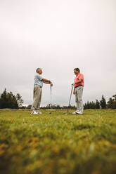 Zwei ältere Golfer stehen mit ihren Golfschlägern auf dem Grün und unterhalten sich zwischen den Übungseinheiten. - JLPSF16674