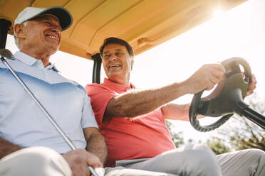 Niedrige Einstellung von zwei älteren Männern, die in einem Golfwagen fahren. Zwei männliche Golfer in einem Wagen, die an einem sonnigen Tag eine Runde Golf spielen. - JLPSF16692