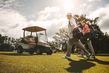 Ältere Golfer, die mit ihren Golftaschen gemeinsam über den Golfplatz gehen. Ältere Golfer, die nach dem Spiel spazieren gehen und sich unterhalten. - JLPSF16695