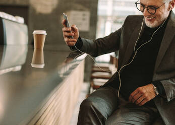 Happy reifen Geschäftsmann trägt Kopfhörer hören Lied von seinem Smartphone im Café. Lächelnde Geschäftsmann im Café hören Musik mit Telefon. - JLPSF16698