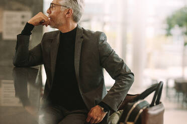 Porträt eines älteren Geschäftsmannes, der in einem Café sitzt. Ein älterer Mann im Geschäftsanzug schaut weg, während er in einem Café sitzt. - JLPSF16701