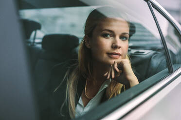 Confident young businesswoman sitting on back seat of a taxi and looking outside the window. Female executive travelling by a car. - JLPSF16707