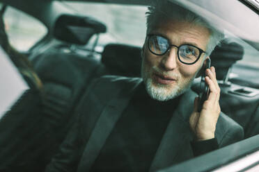 Happy businessman sitting on back seat of a car and talking on the mobile phon. Mature man travelling by a taxi and making phone call. - JLPSF16709