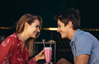 Romantisches Paar bei einem Date, das im Freien sitzt und sich einen Milchshake mit zwei Strohhalmen teilt. Paar, das sich in einem Restaurant ansieht. - JLPSF16725