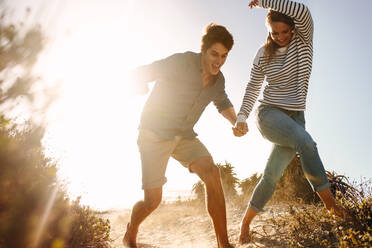 Paar spielt und läuft in den Sand in der Nähe von Meer Ufer an einem sonnigen Tag. Glückliches Paar genießen und Spaß haben am Strand halten Hand mit Sonne Flare im Hintergrund. - JLPSF16734