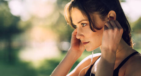 Close up of a female athlete wearing earphones outdoors. Woman listening to music during workout. - JLPSF16751