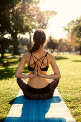 Fitness woman practising meditation yoga outdoors. Fitness female doing Pashchima Namaskarasana yoga sitting on mat at the park. Rear view shot of female practising reverse prayer position yoga. - JLPSF16753