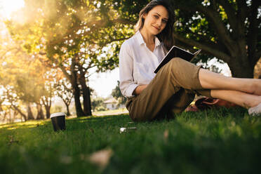 Hübsche junge Frau sitzt im Park mit einem Buch. Kaukasische Frau liest einen Roman im Park. - JLPSF16759