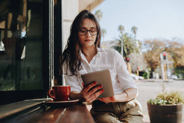 Frau, die in einem Café sitzt und an einem digitalen Tablet arbeitet. Geschäftsfrau, die mit einem Kaffee am Tresen eines Cafés sitzt und einen Tablet-Computer benutzt. - JLPSF16760