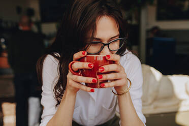 Nahaufnahme einer Frau mit Brille, die eine Kaffeetasse hält und wegschaut. Frau mit Kaffeetasse sitzt in einem Café. - JLPSF16761