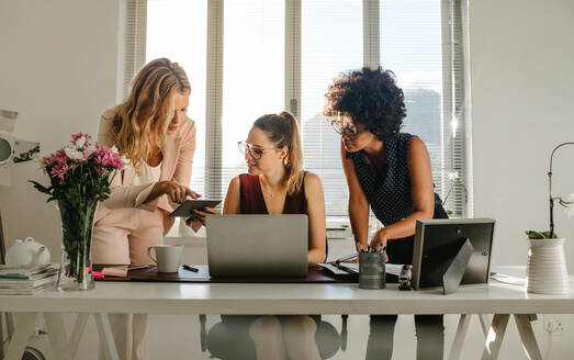 Gruppe junger Geschäftsfrauen, die im Büro zusammenarbeiten. Frauen in Freizeitkleidung, die ein digitales Tablet und einen Laptop in einem modernen Büro benutzen. - JLPSF16766