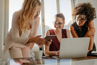 Three beautiful creative business woman working with laptop and watching something on tablet in office. Group of businesswoman working over a new project at startup office. - JLPSF16768